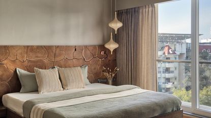 A bedroom with a large double bed next to a window. Beside the bed are two pendant lights hanging elegantly above a side table 