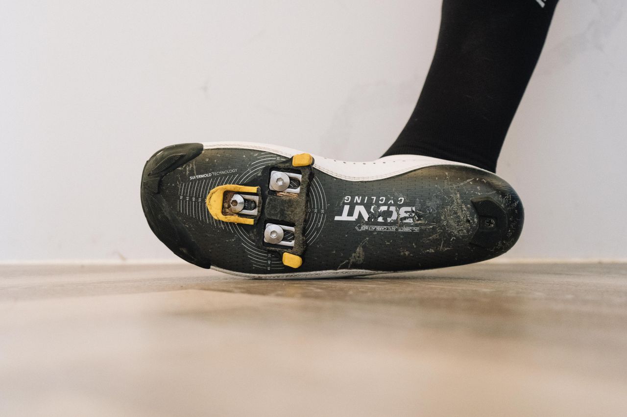 A close up of a white cycling shoe with a black socked foot in it