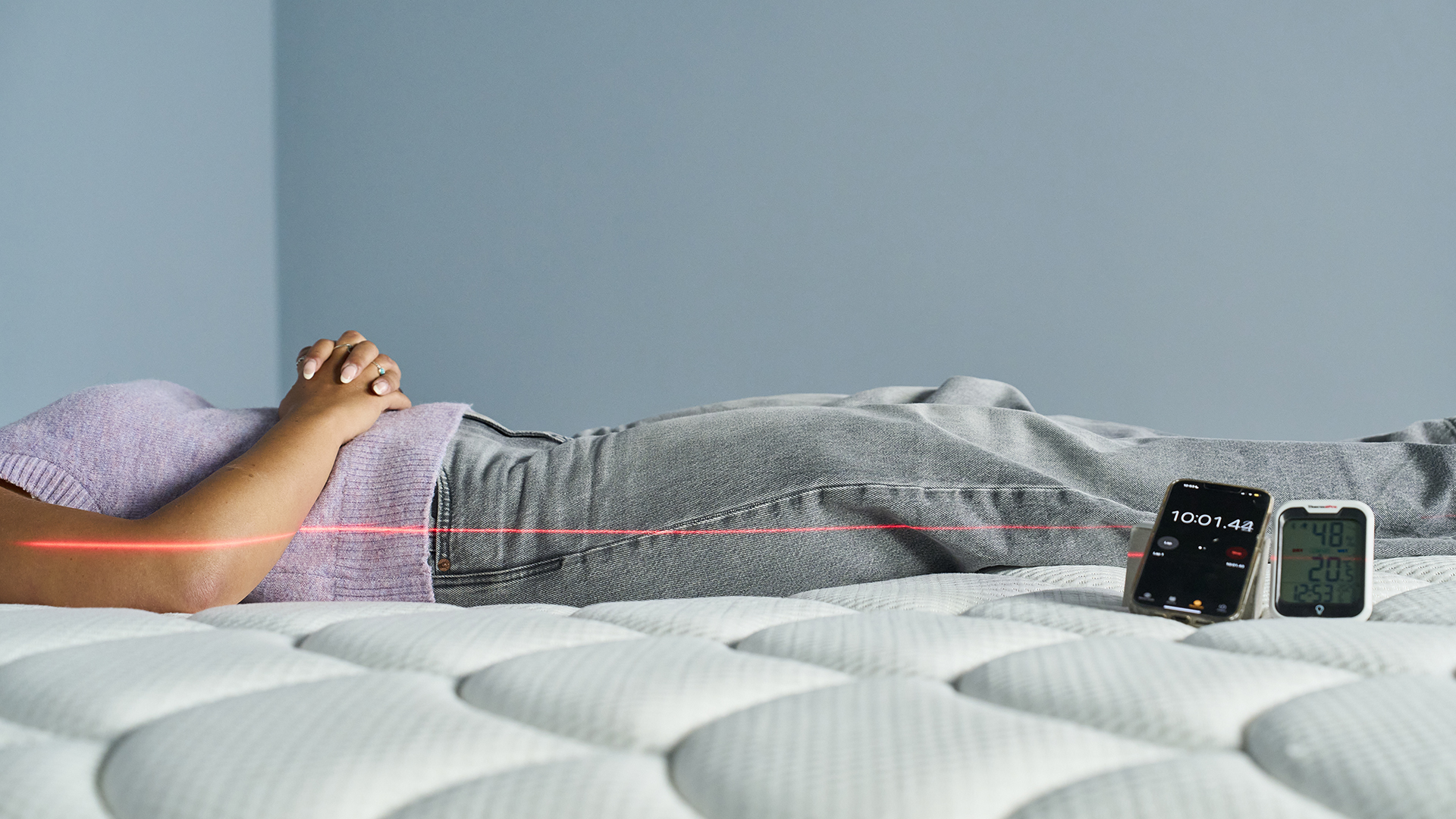 A Tom's Guide Tester lies on her back on the DreamCloud Classic mattress. A red line from a laser is seen along the side of her body to measure how straight her spine is.