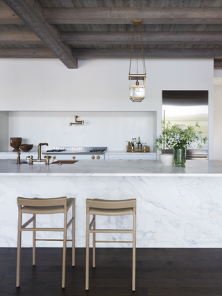Minimalistic kitchen with marble island, stools and brass fittings