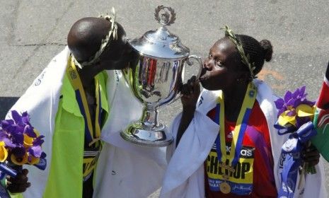 The winners of the men&amp;#039;s and women&amp;#039;s divisions of the 2012 Boston Marathon kiss the trophy during the awards ceremony Monday.