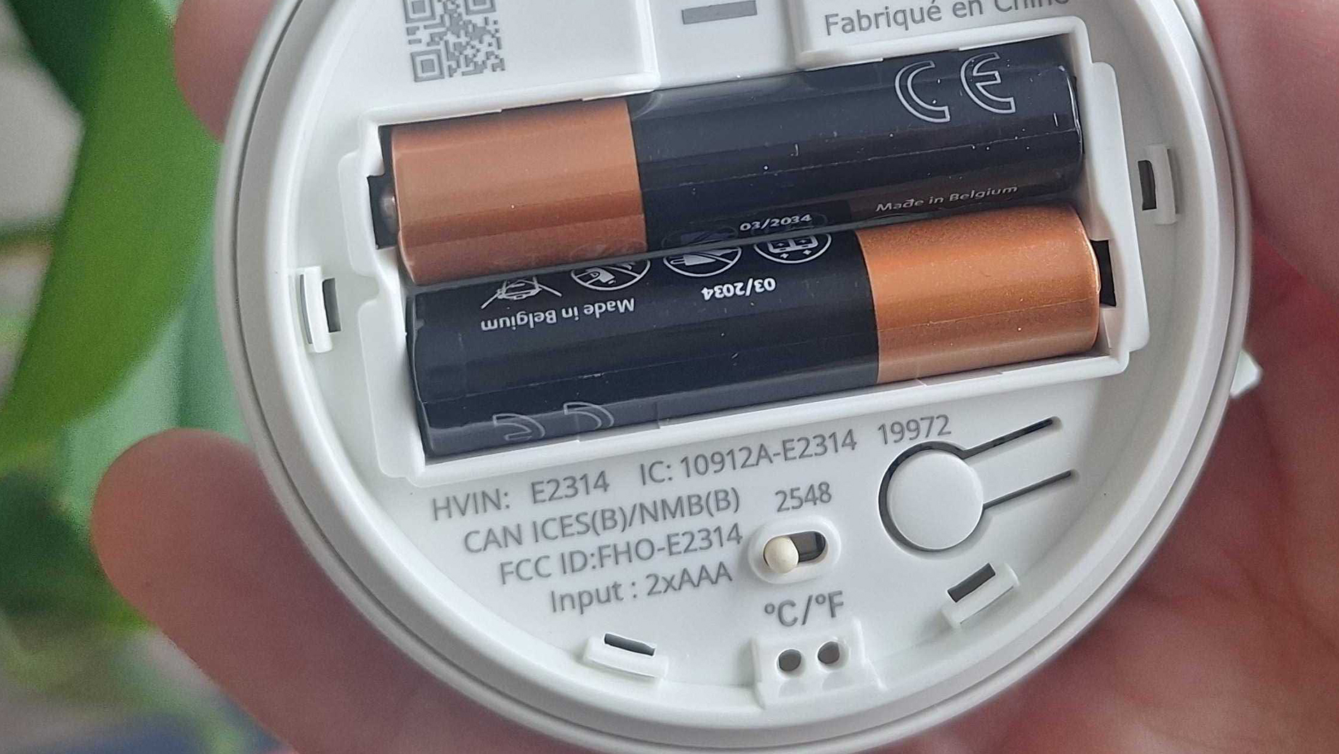 IKEA Timmerflotte temperature and humidity sensor on a wooden table, with back cover removed to show 2 AAA batteries and a celcius-fahrenheit toggle