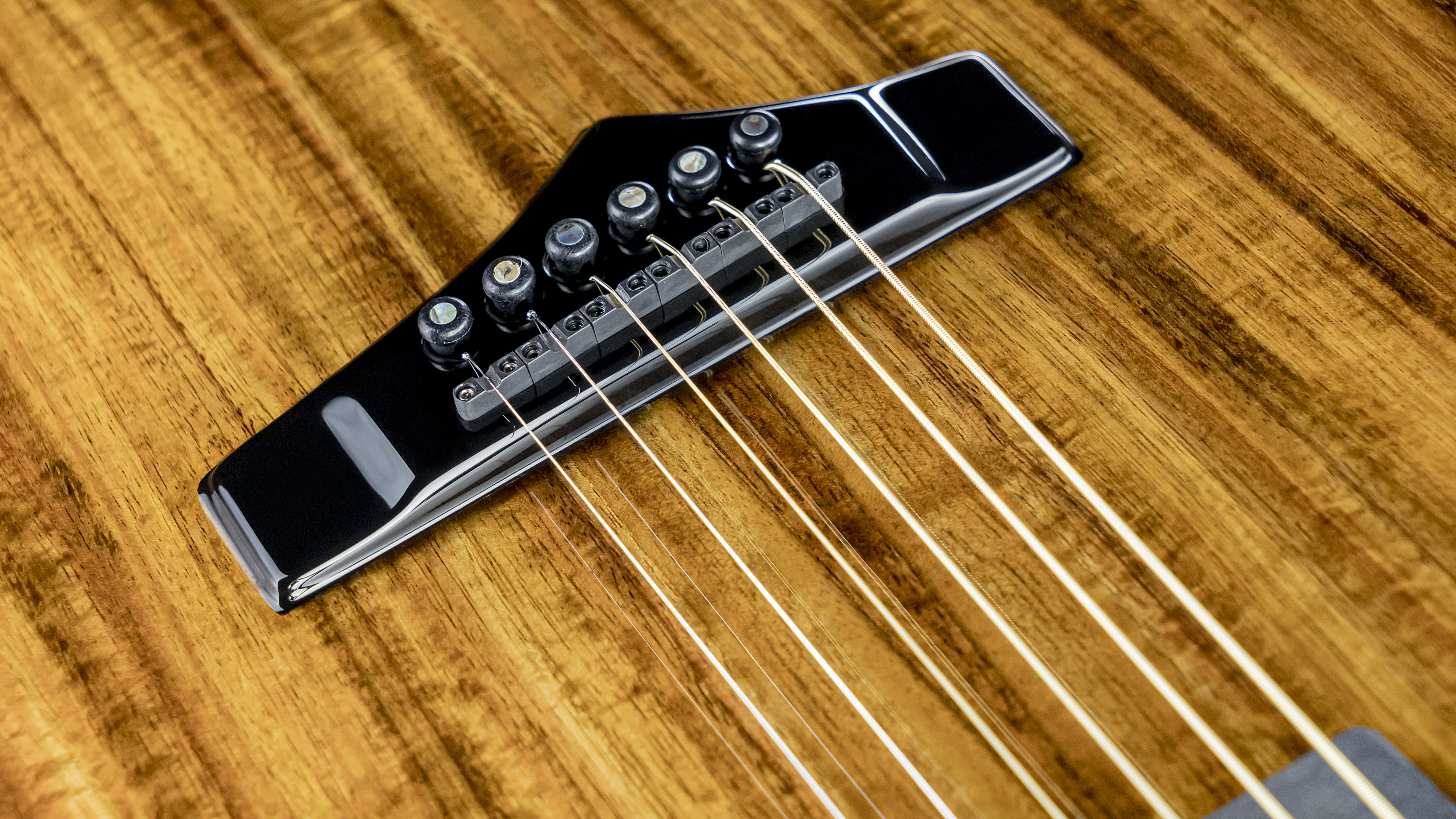 A close-up on the X10's Graphtech Ghost bridge with koa veneer option 