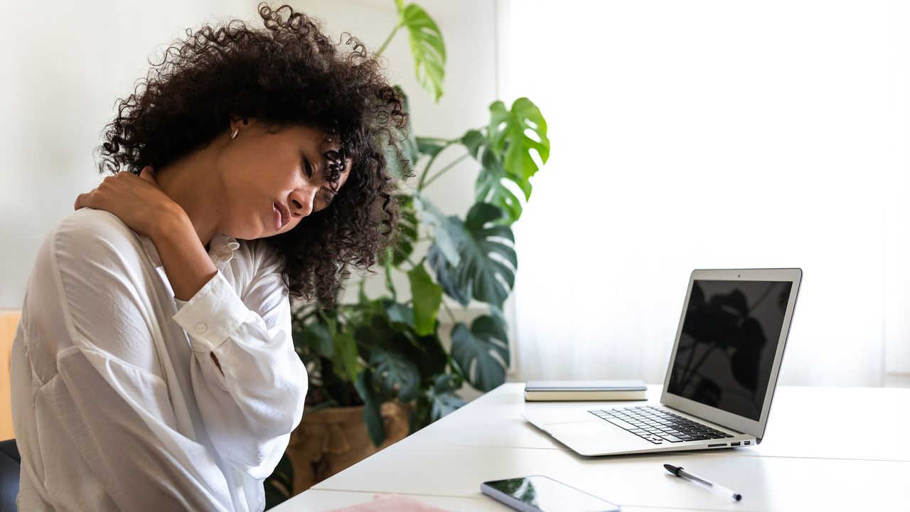 Woman sat at work desk rubbing tension knot in her shoulder