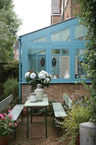 a sky blue painted garden room in a garden with an outdoor dining table and benches