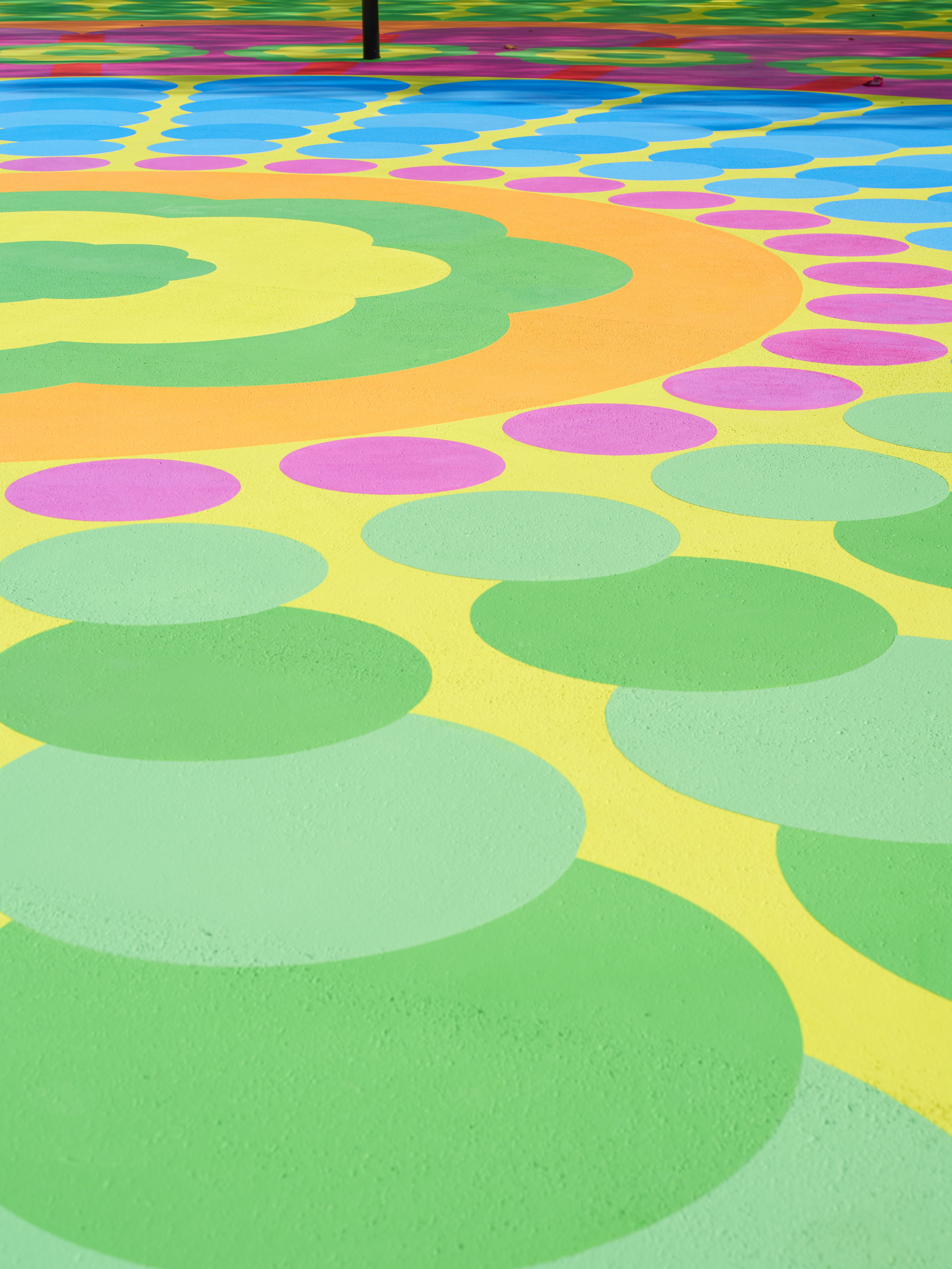 Aerial view of a colorful, abstract mural in tones of pink, red, green, yellow, and blue as seen up close on a sunny day.