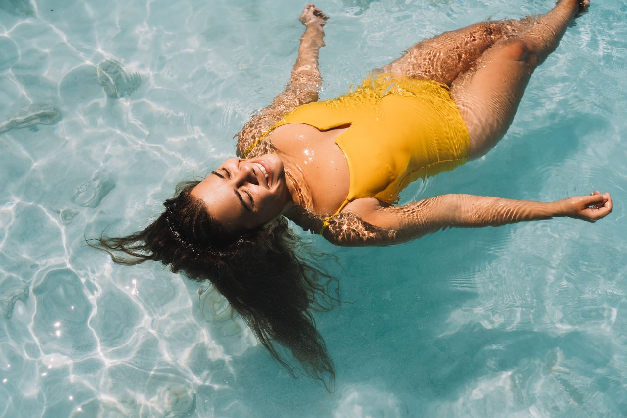 A relaxed woman wearing a yellow swimsuit floating in a pool. 