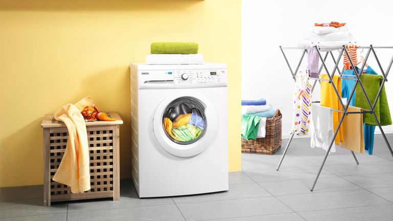 A washing machine against a yellow wall with clothes horse and storage basket - zanussi