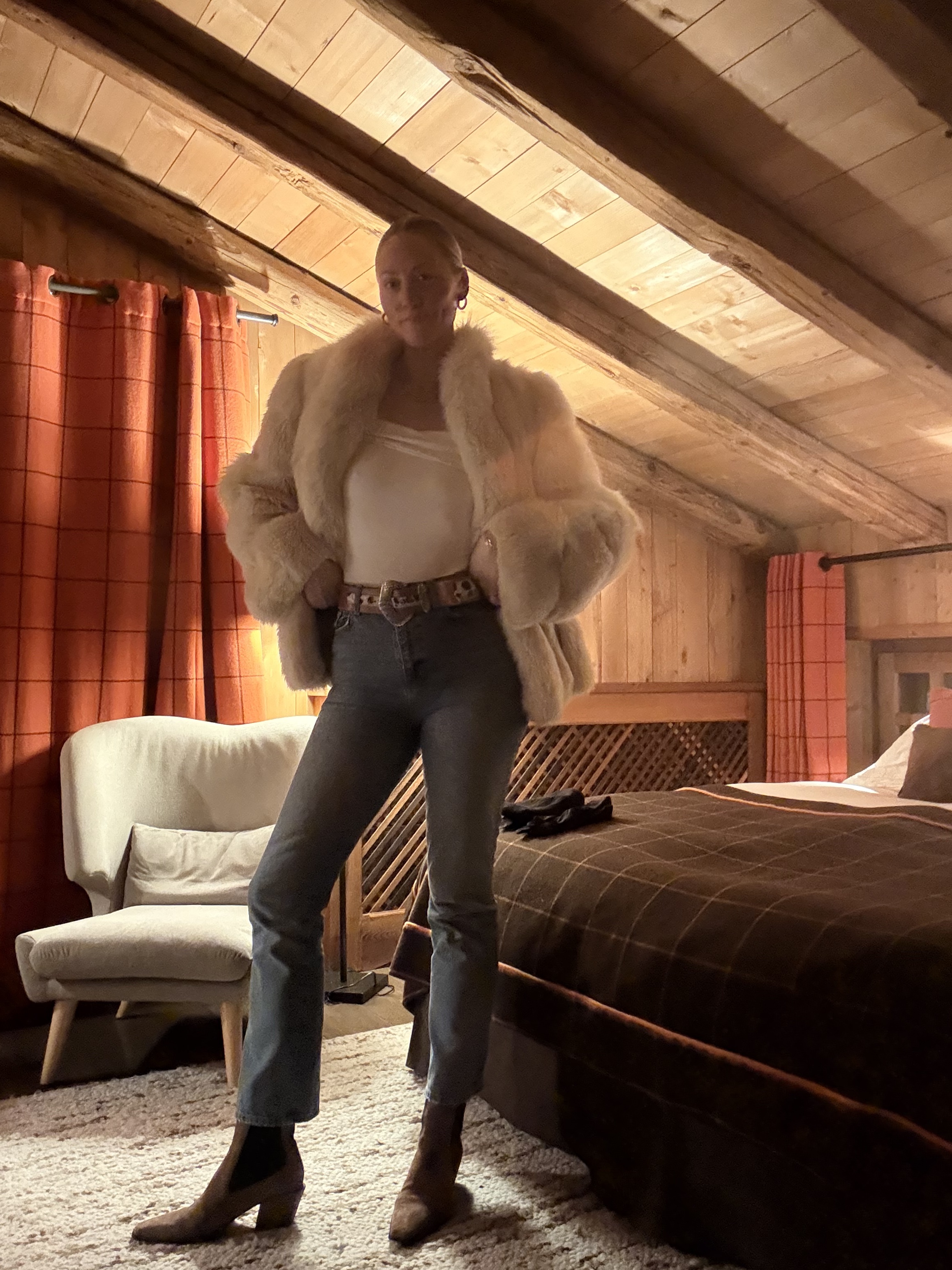 Brooke Ely Danielson in a cabin-like room wearing high-waisted jeans, a fur jacket, and boots