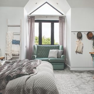Grey carpetted floor with light grey patterned rug, in front of window and blue couch and next to bed with dark grey and patterned bedding