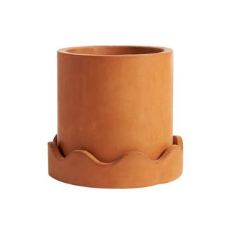 An orange terracotta plant pot with a wavy scalloped trim at the bottom of it