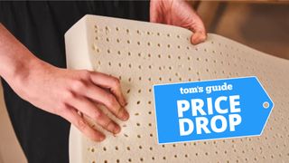 A hand feels a latex mattress topper with a blue deals label in the foreground.