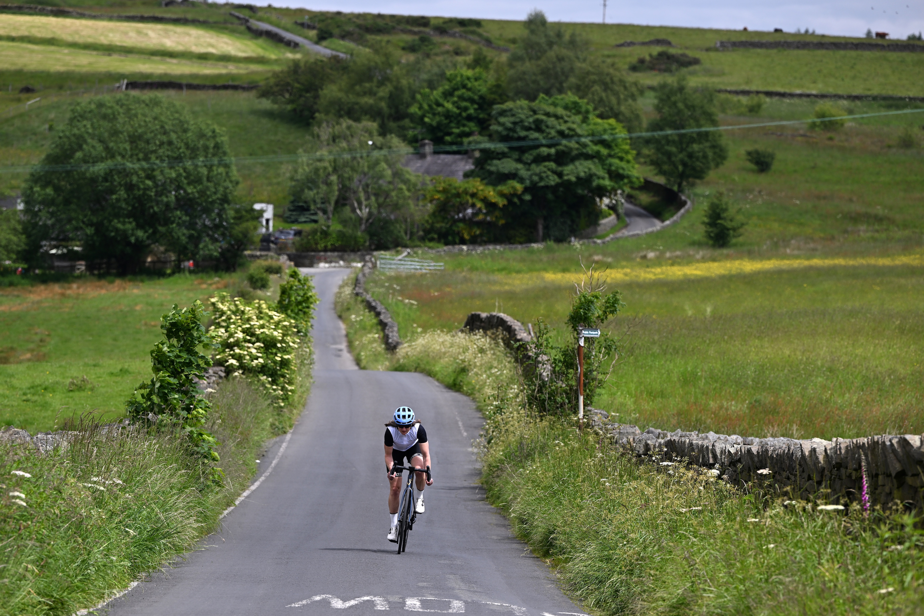 Female cyclist riding between fields towards camera