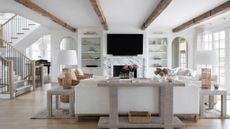 living room with white walls and white sofa, wood beams in ceiling and TV above marble fireplace