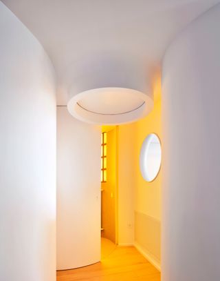 White curved-wall hallway leading to yellow bathroom with porthole window looking out to living room