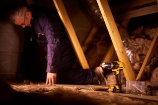 A man works inside his loft with an impact driver nearby