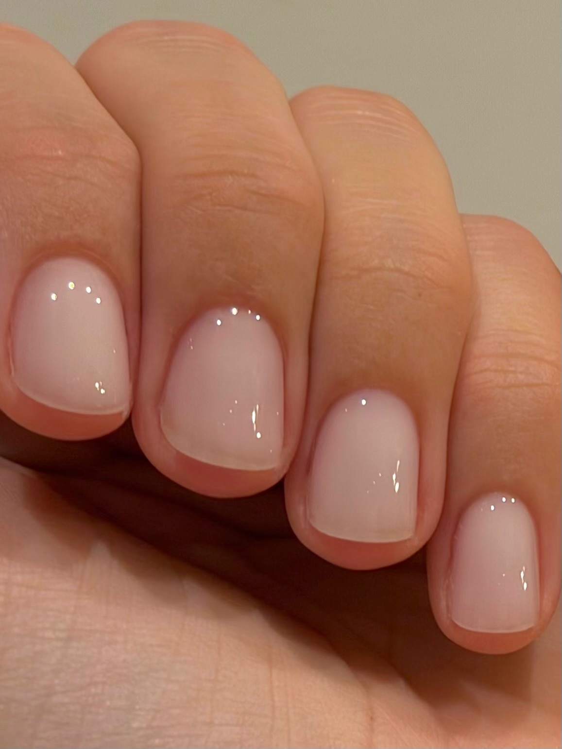 A close-up of a short, super glossy, sheer milky manicure