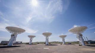 six large white radar dishes point to the sky in the desert under a bright sun