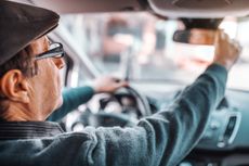 A senior man adjusts his review mirror while driving.