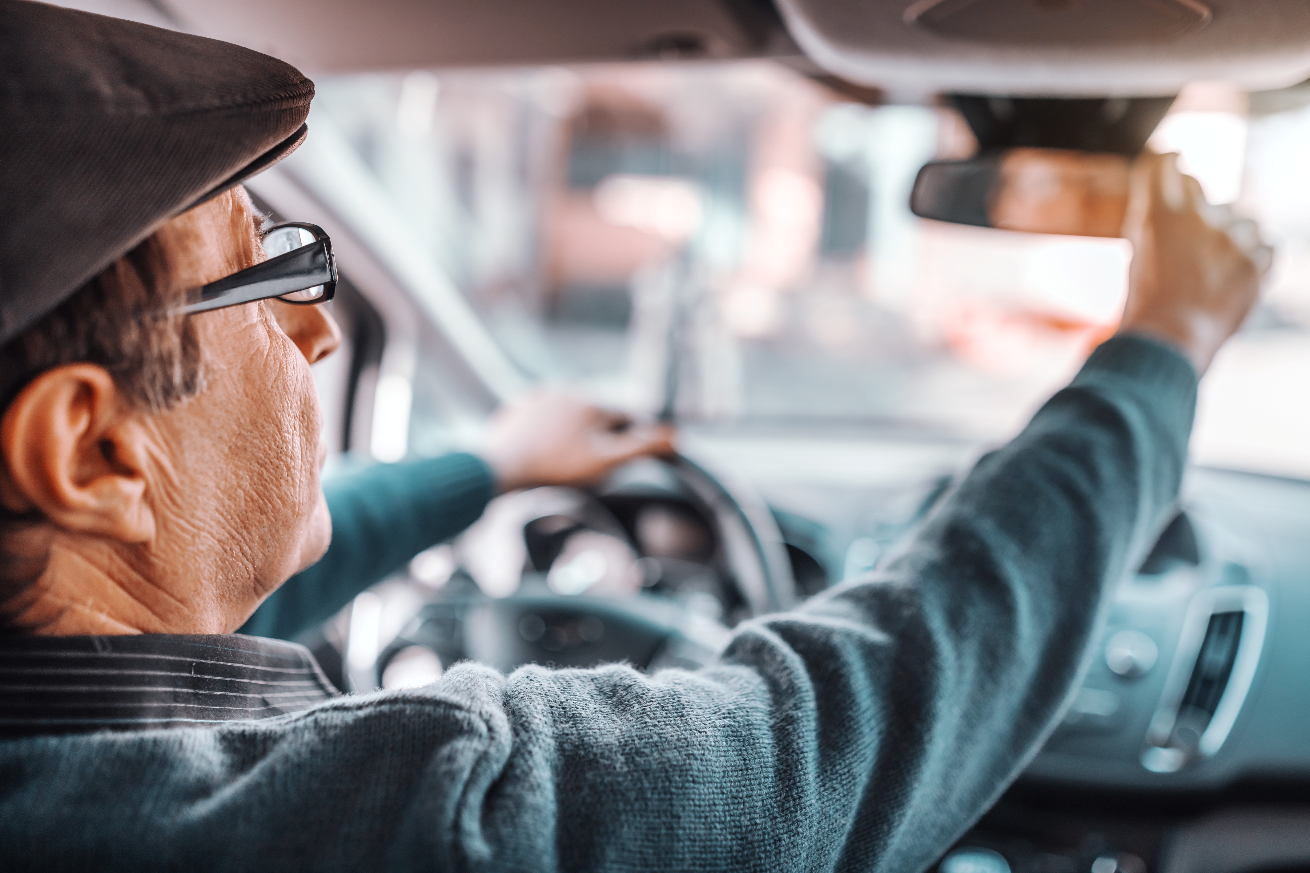 A senior man adjusts his review mirror while driving.