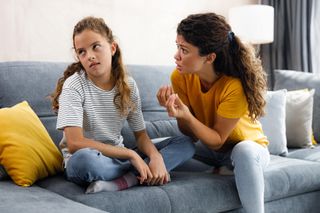 Frustrated single mother talking to her rude girl who is ignoring her at home