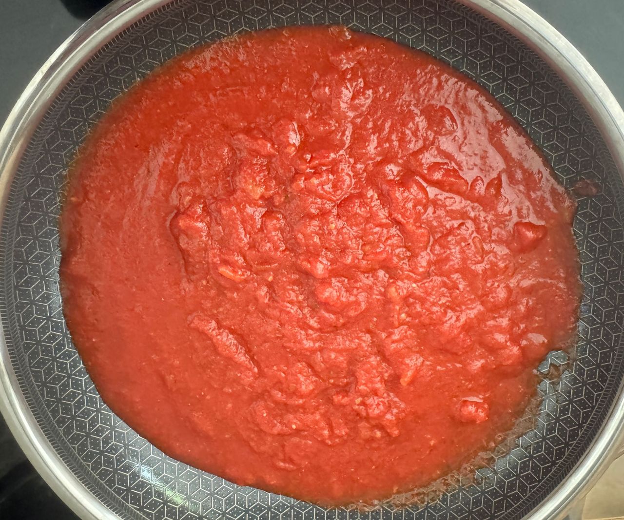 Red tomato sauce in a black lined stainless steel frying pan, viewed from above.