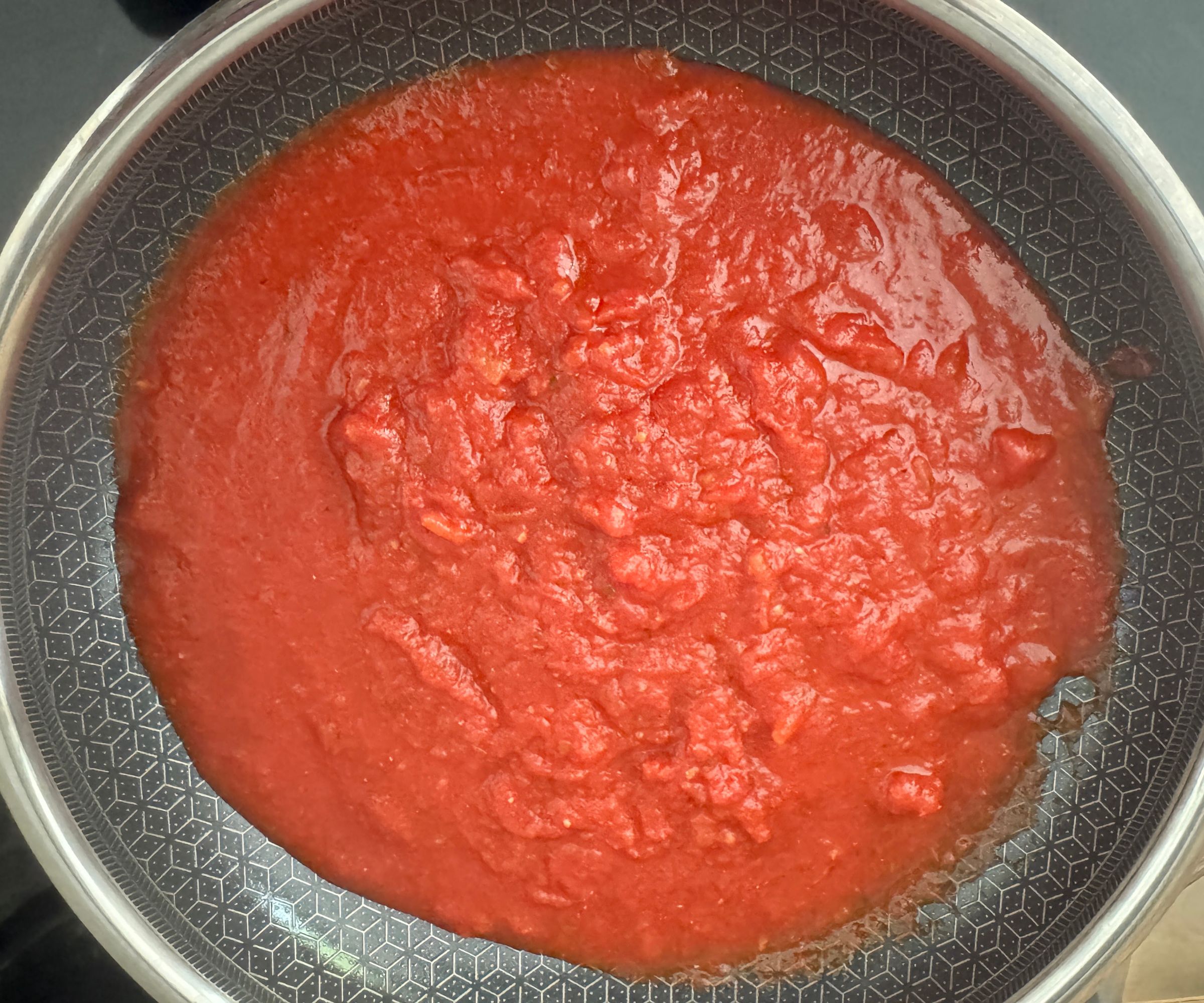 Red tomato sauce in a black lined stainless steel frying pan, viewed from above.