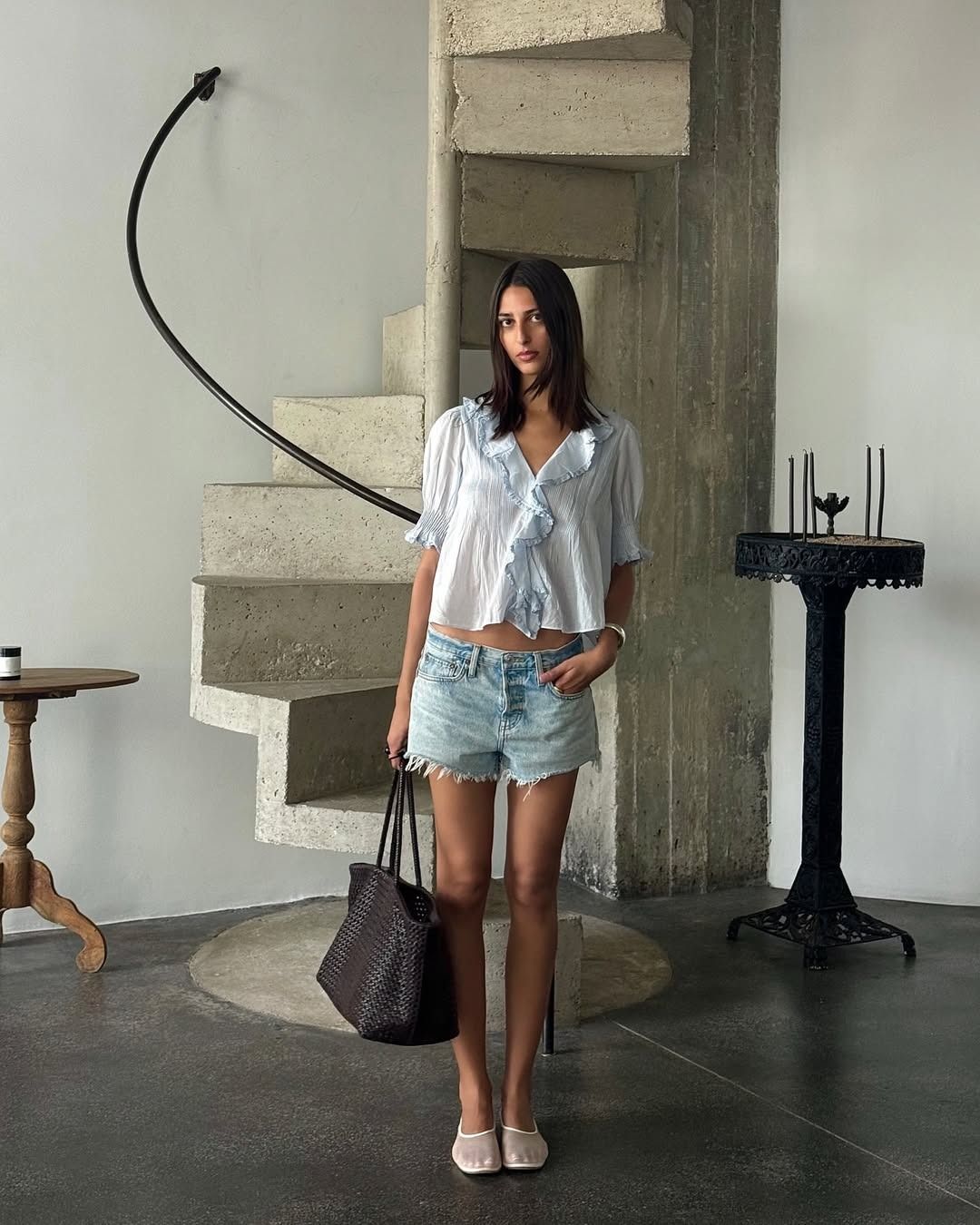 Influencer wearing denim shorts with a ruffled blouse and mesh flats