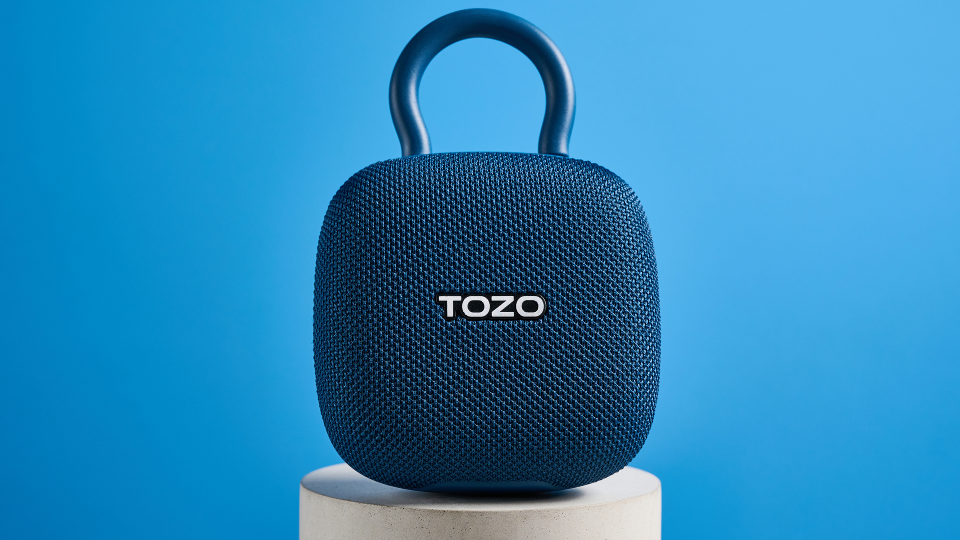 Tozo PE1 speaker in blue with built-in clip photographed on a blue background.