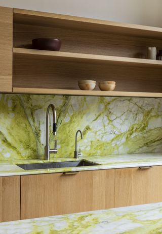 A kitchen with marble backsplash with bright green veining, timber cabinetry and open shelving