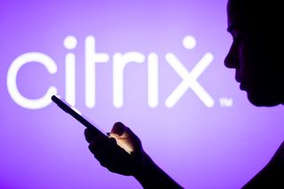 Citrix Systems logo is seen in the background of a silhouetted woman holding a mobile phone
