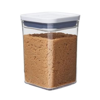 A rectangular plastic container with light brown sugar in it and a white lid with a dark blue trim