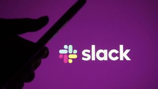 Slack logo on purple background with silhouette of hand using mobile phone in foreground