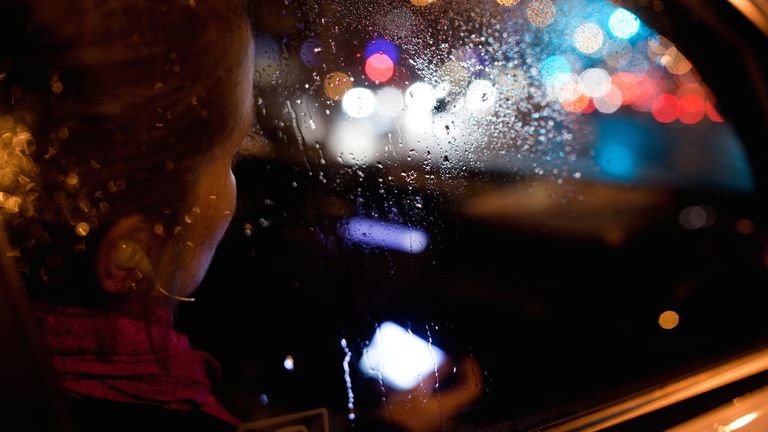View of woman through car window, raining at night