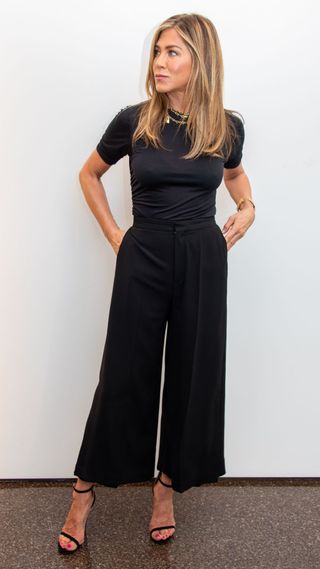 Jennifer Aniston wearing black culottes, black t-shirt and black heels