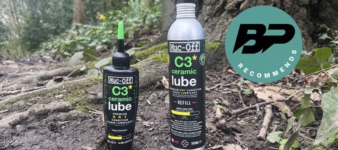 Two bottles of bike chain lube on muddy ground in wood