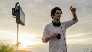Damien Chazelle wearing headphones and directing on the set of Babylon.