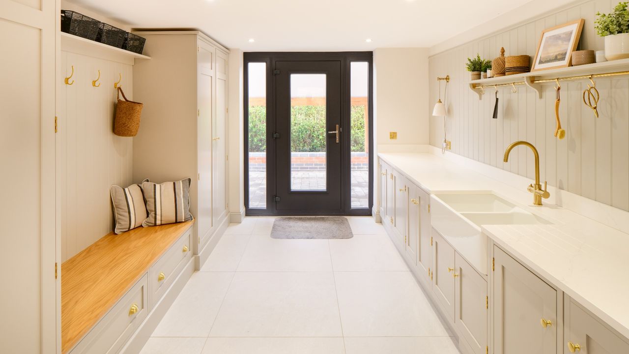 a modern, neutral laundry room with an entryway bench, a black door, and a sink