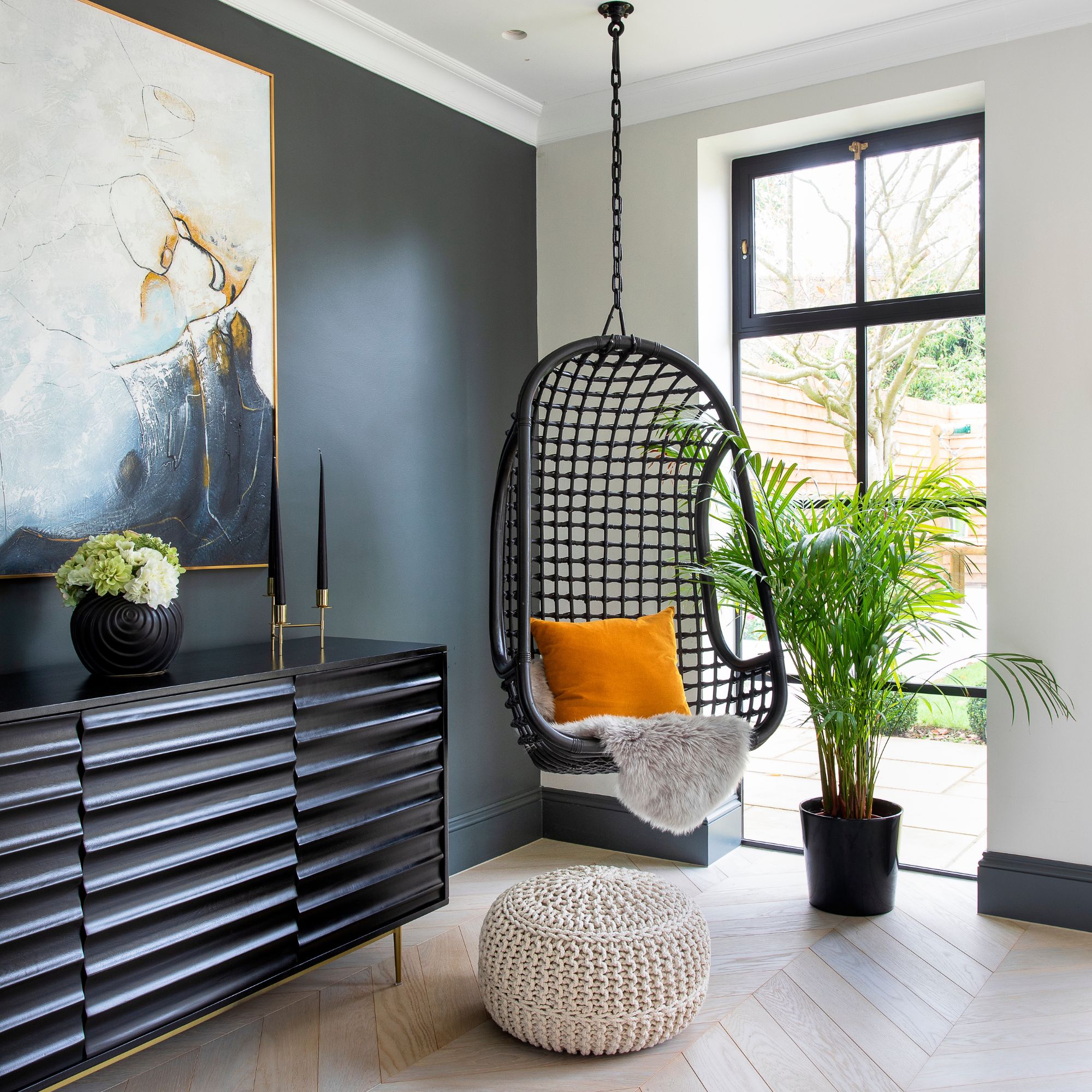 A monochrome corner with a hanging mesh back chair with an orange accent cushion
