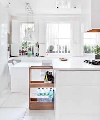 An example of small kitchen storage ideas showing a white kitchen with a large white island with smart pull-out storage