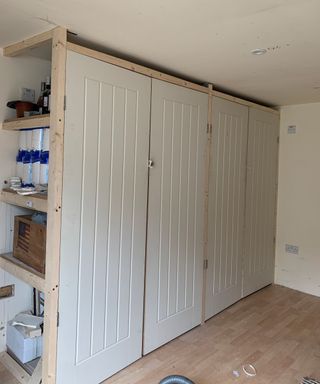 A garden outbuilding with laminate flooring, wooden frames, MDF shelves and three wooden doors with paneled detail