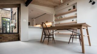 pale grey microcement floor in kitchen diner extension with white walls, large picture window and wooden table table and chairs