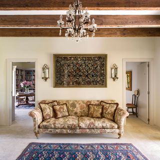living room with floral print sofa and beams with chandelier and two doorways behind