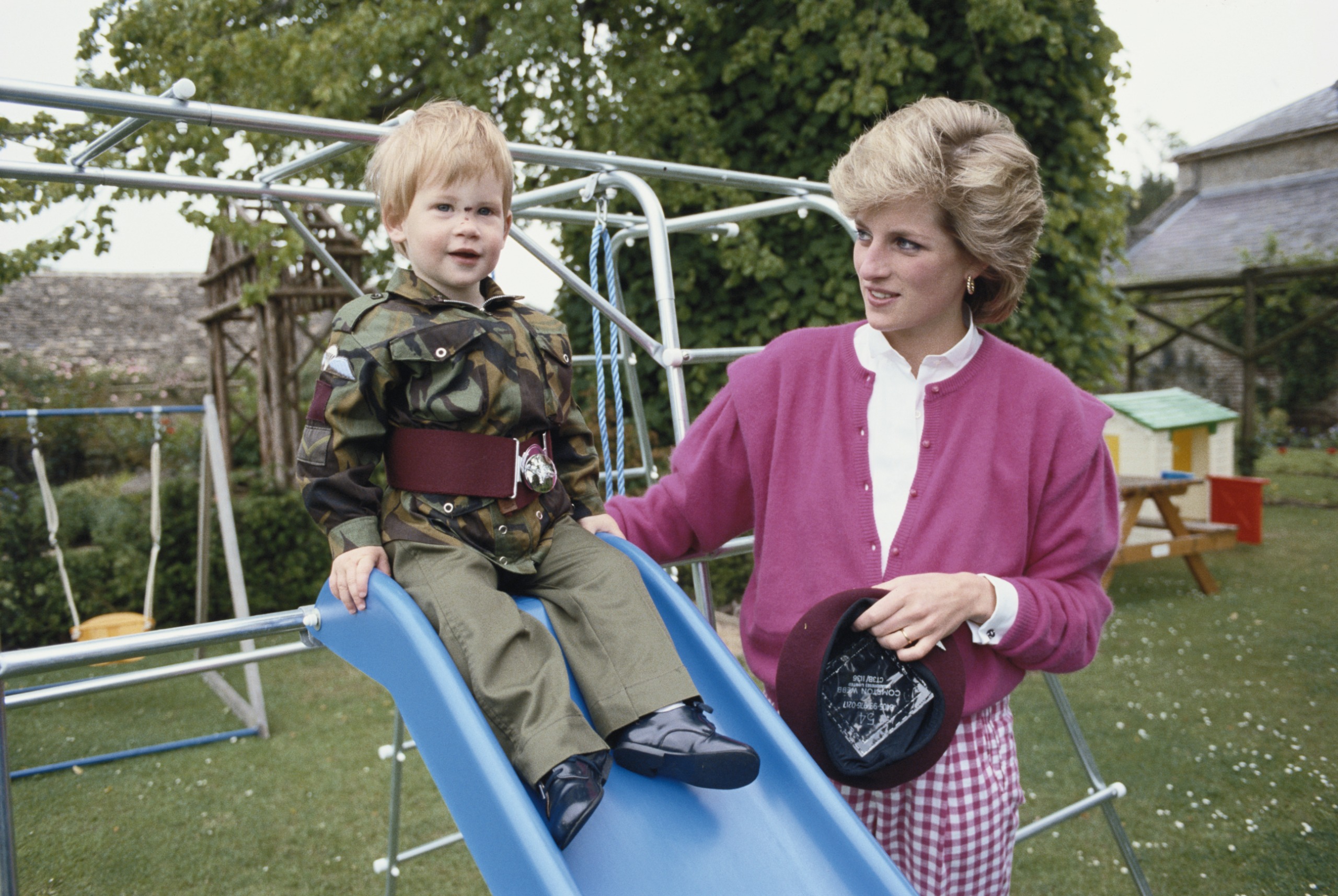 Prince Harry sitting on a slide in an army costume next to Princess Diana