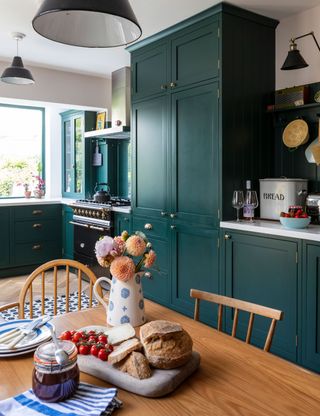 A green Shaker kitchen with pine dining table and large pantry cupboards