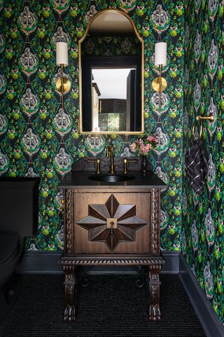 A powder room with green wallpaper, a dark wooden sink pedastal, and a black toilet
