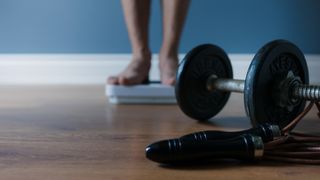 Man standing on scales with dumbbells nearby