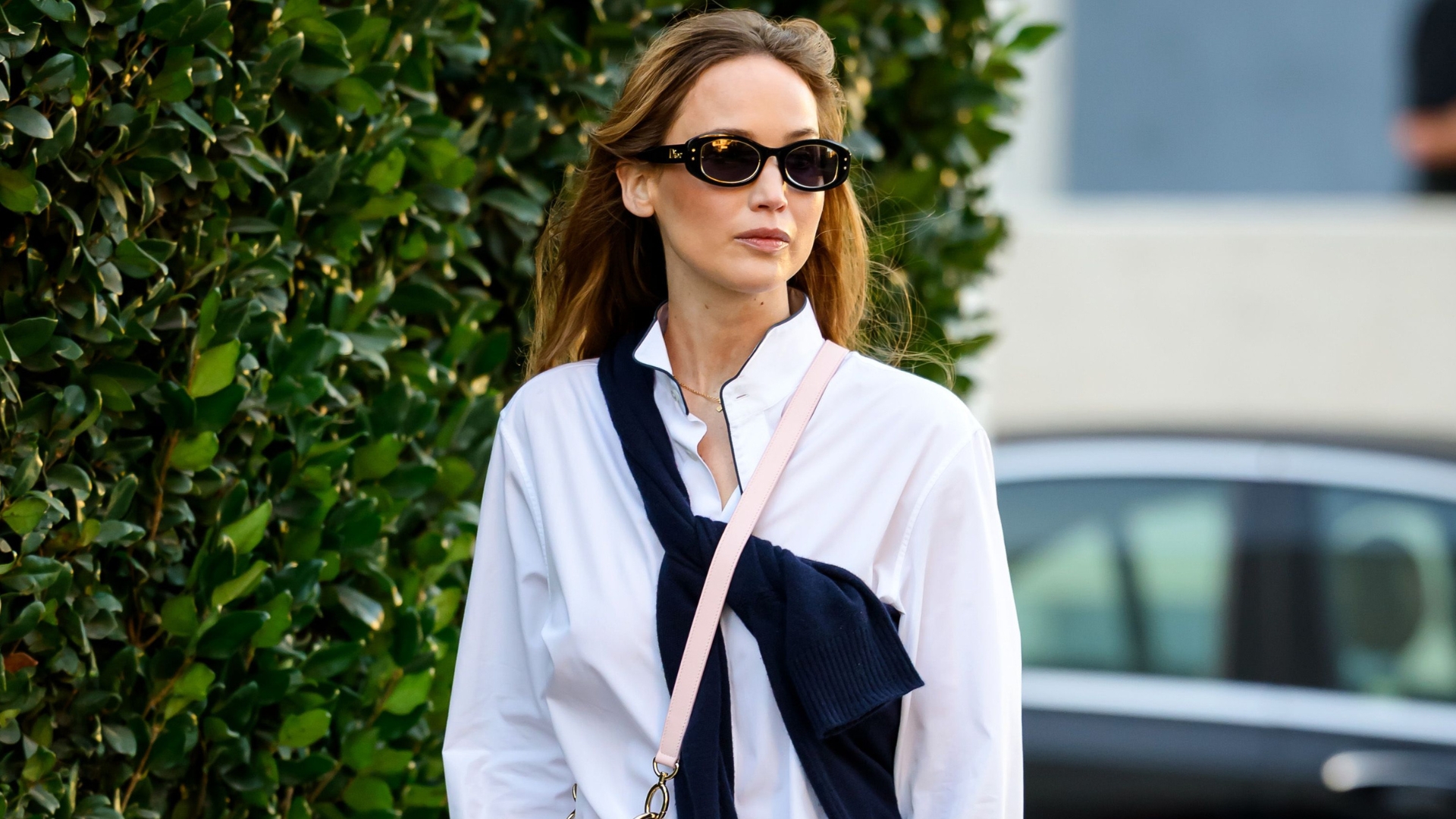 Jennifer Lawrence walks down the street wearing Dior's Cigale handbag with a white button-down shirt, black trousers and black flip-flips.