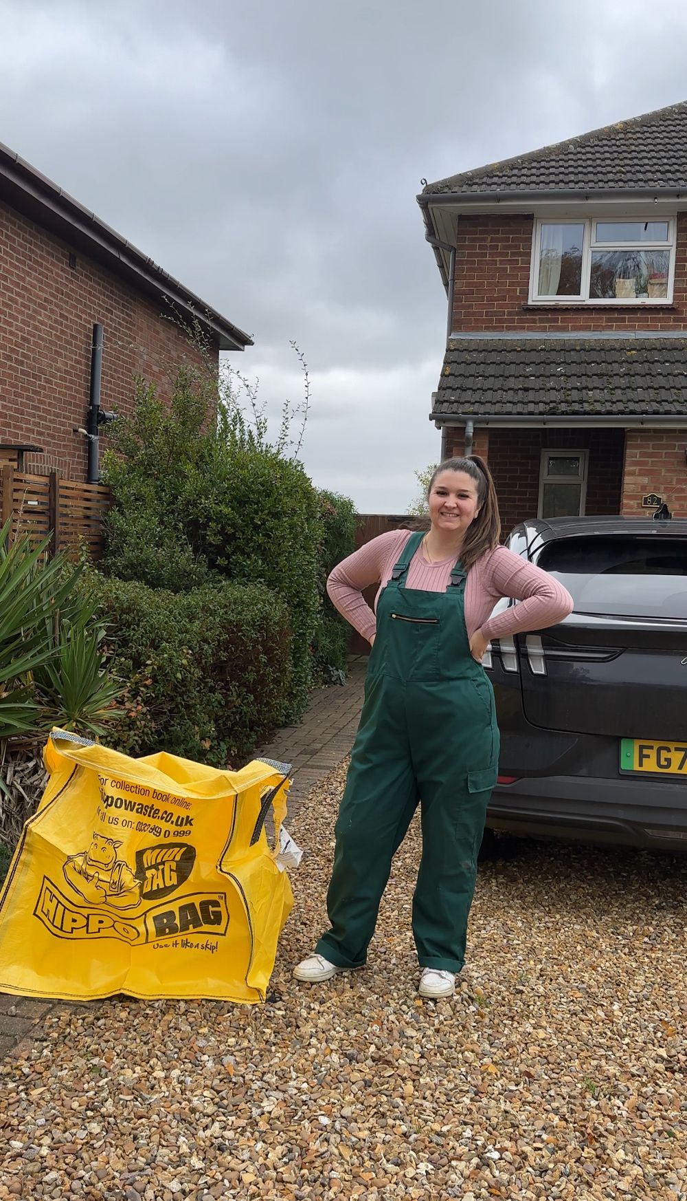 A woman stands next to a yellow bag of DIY tools outside her house