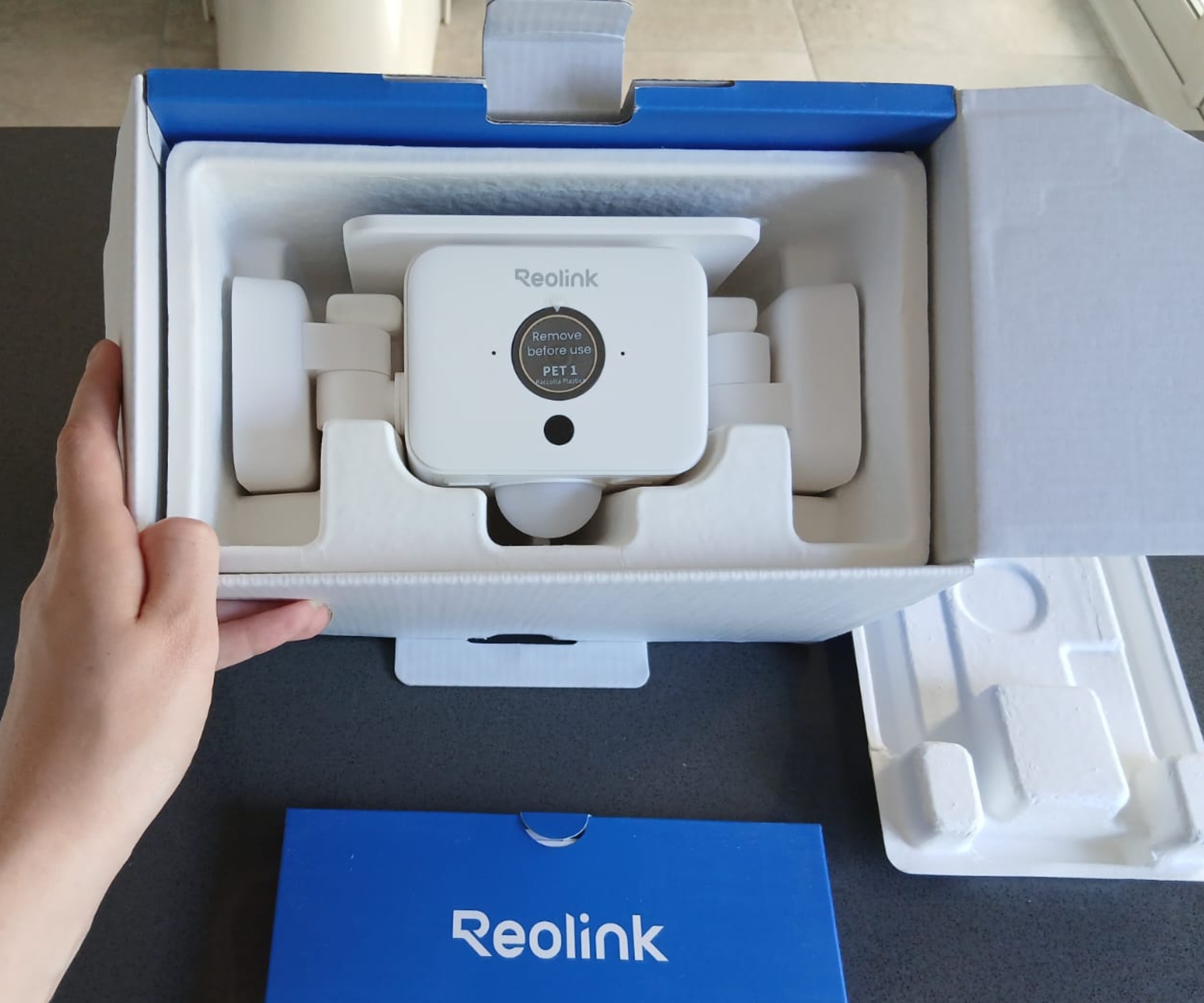 Reolink floodlight camera in unboxed packaging, foam insert, hand lifting the box lid open.